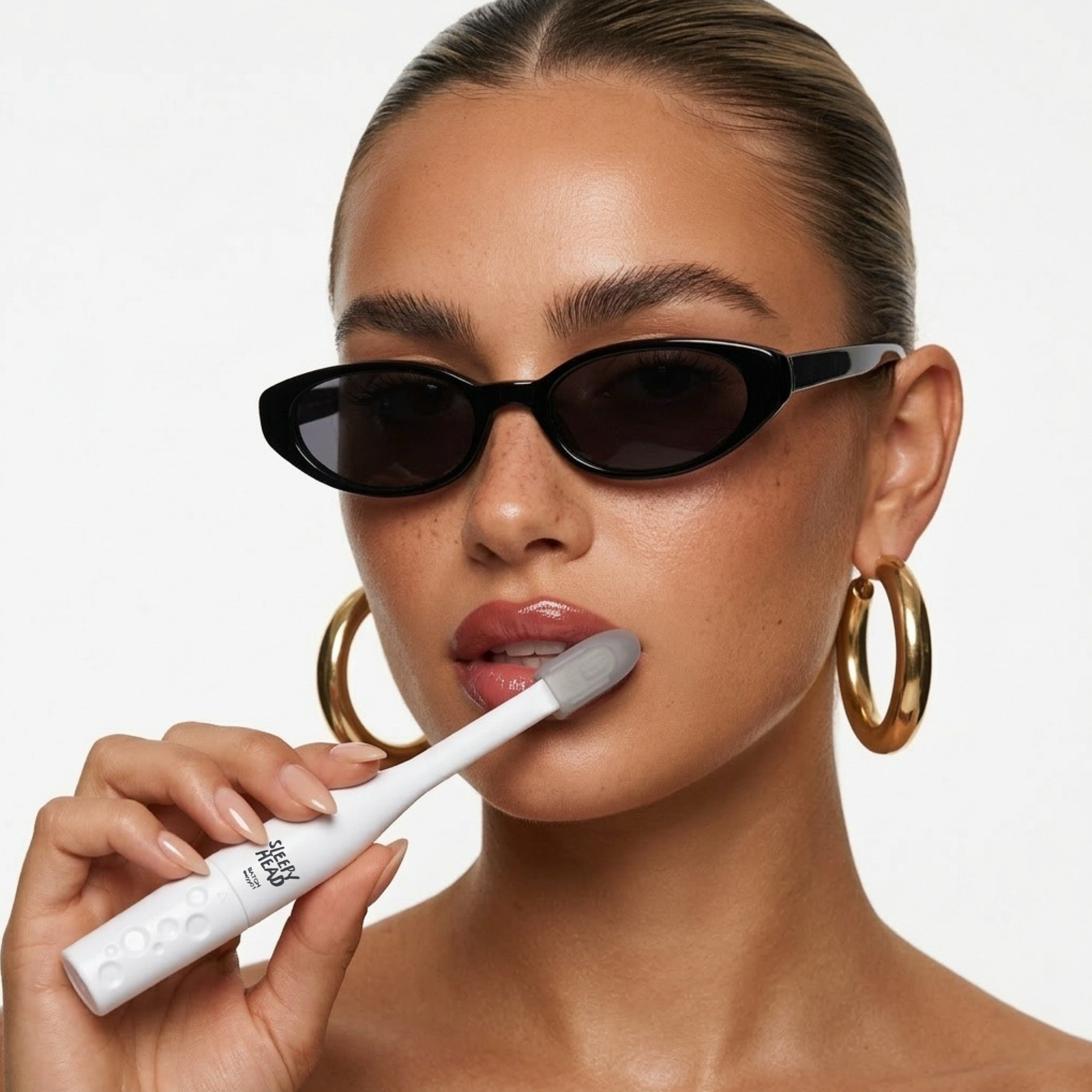Woman wearing sunglasses and gold hoop earrings, holding a white electronic toothbrush.